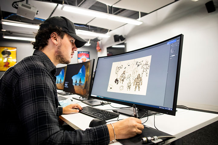 A student working on animated character modeling on a large computer screen